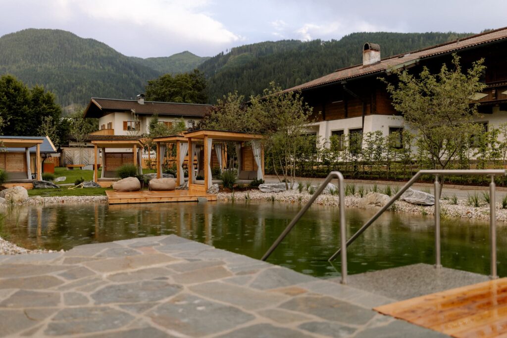 Naturbadeteich mit Loungeliegen im Garten des Hotels